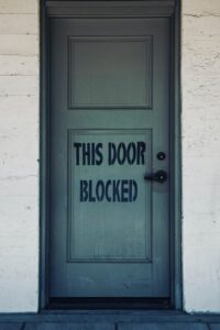 A picture of a door that says, 'this door blocked' which resembles being stuck in business